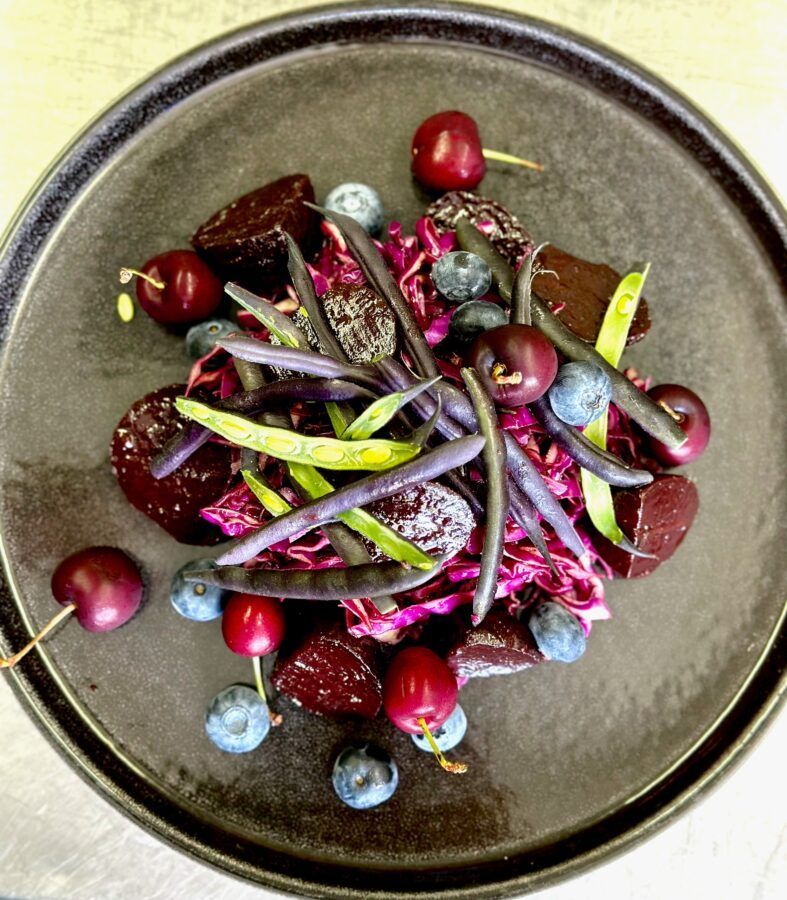 Dark plate with purple cabbage, roasted beets, purple beans, cherries, and blueberries