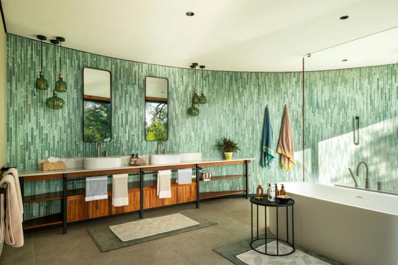 Spacious bathroom with green vertical tile walls, double vanity, freestanding tub, and pendant lighting