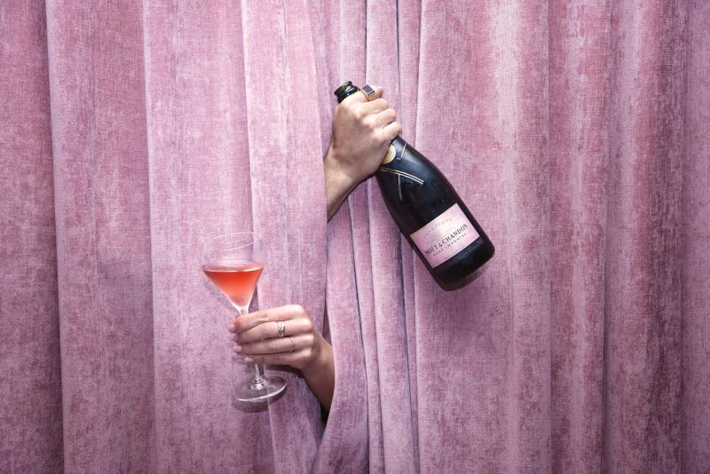 A bottle and glass of Rosé Champagne in front of a velvet drape curtain