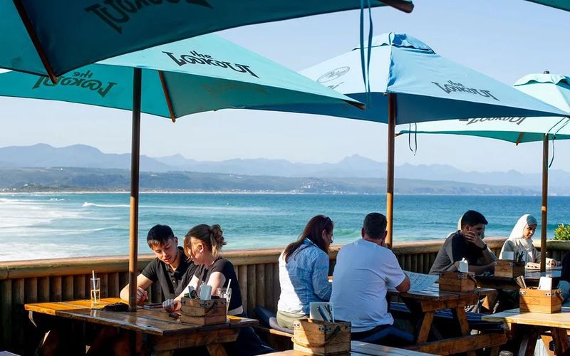 Outdoor dining terrace with large umbrellas and tables overlooking a beach and ocean in Plettenberg Bay