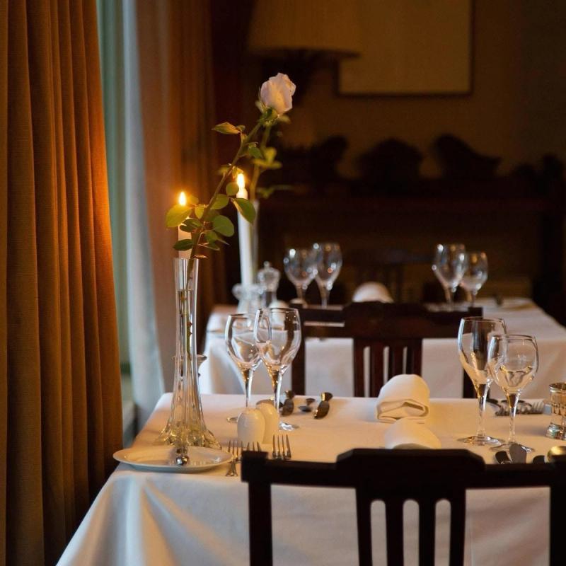 Elegant dining table set with wine glasses, white rose and candles in a dim room