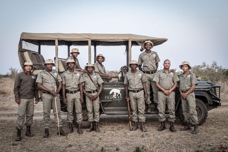A group of Rhino Guardians from Tracker Academy stand in front of a safari vehicle in uniform.