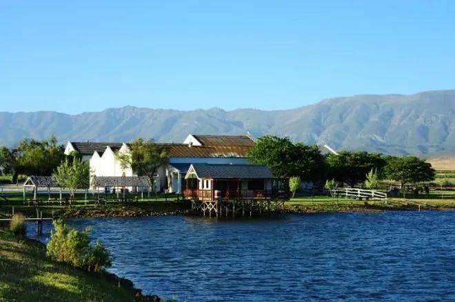 A lakeside house with a deck sits before mountains under a clear blue sky in Robertson.