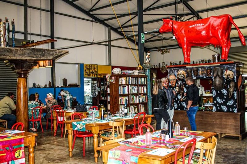 Eclectic dining space in Swellendam features a large red cow sculpture above a decorated bar counter