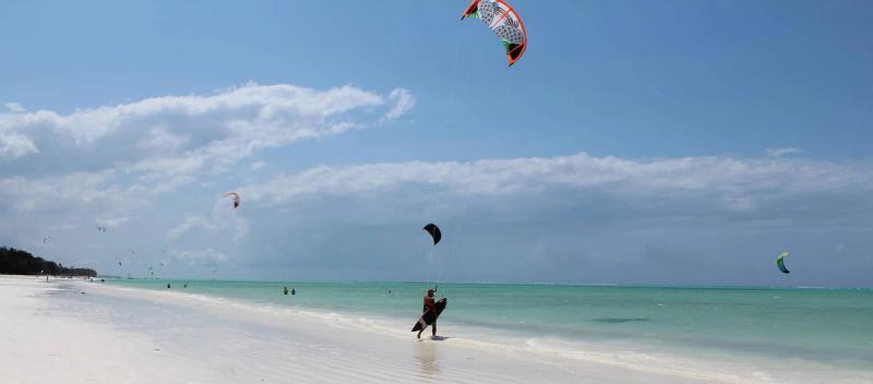 Ein Kitesurfer auf dem Ozean vorm weißen Sandstrand von Sansibar