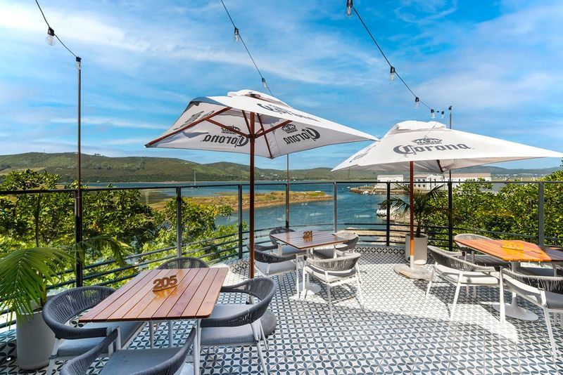 Rooftop terrace with patterned tile flooring, umbrellas, and tables overlooking the Knysna lagoon