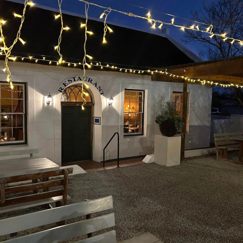 A thatched-roof restaurant entrance in Swellendam lit with string lights at dusk.