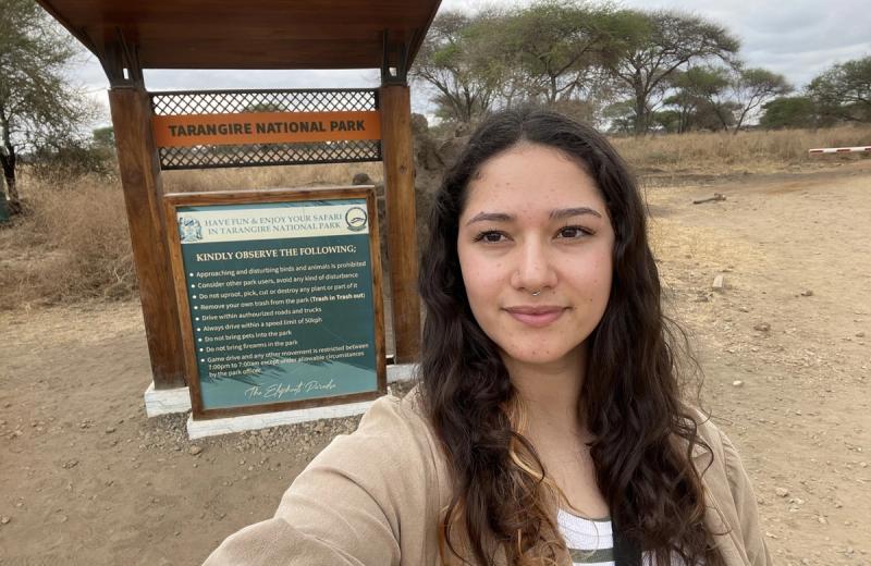 Rhino Africa Travel Expert Laura Hall stands in front of Tarangire National Park sign while on a Tanzania safari