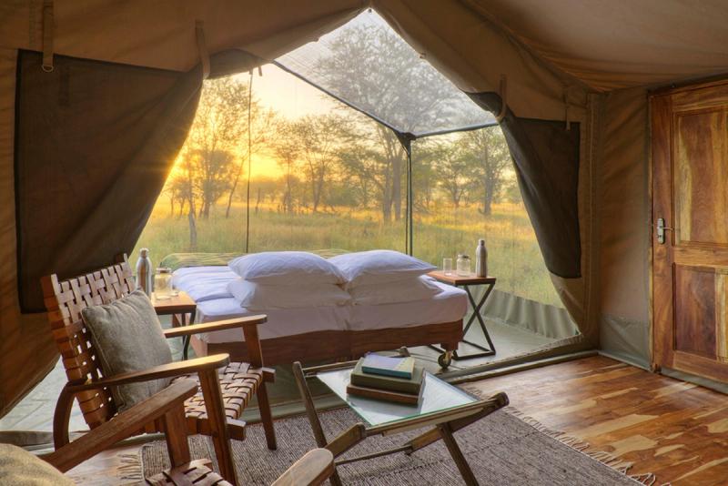 Sunlight spills through mesh panels onto a made-up bed inside one of Tanzania’s mobile tented camps, surrounded by natural textures and thoughtful details.