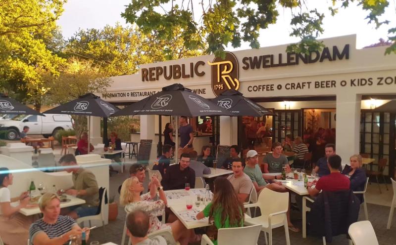 People dining outdoors at Republic Swellendam under umbrellas at dusk