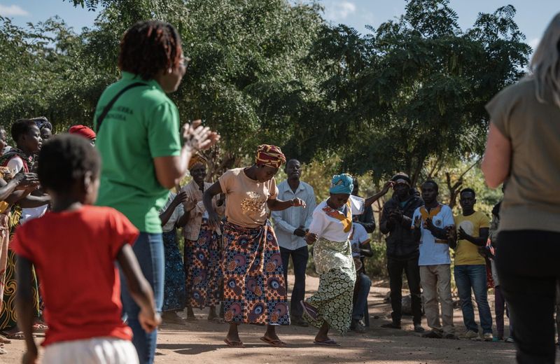A group of local community members dance and clap together outdoors beneath trees, showing the impact in Gorongosa through shared participation, culture, and collective presence.