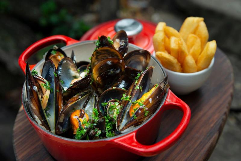 A red pot of steamed mussels with herbs served beside a bowl of chips in Knysna