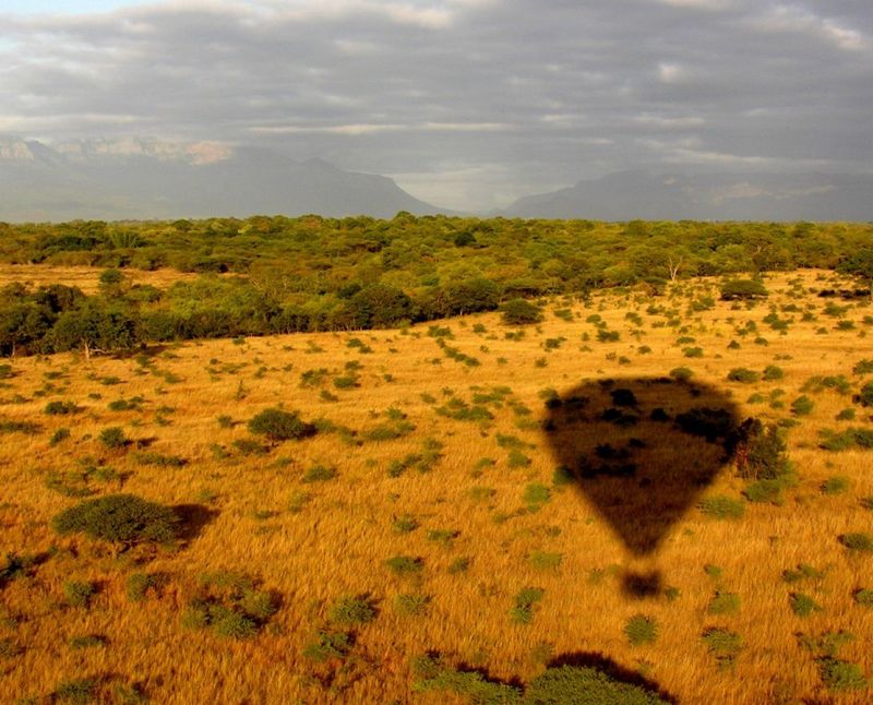 eine braune Landschaft, in der man den Schatten eines Heißluftballons sieht