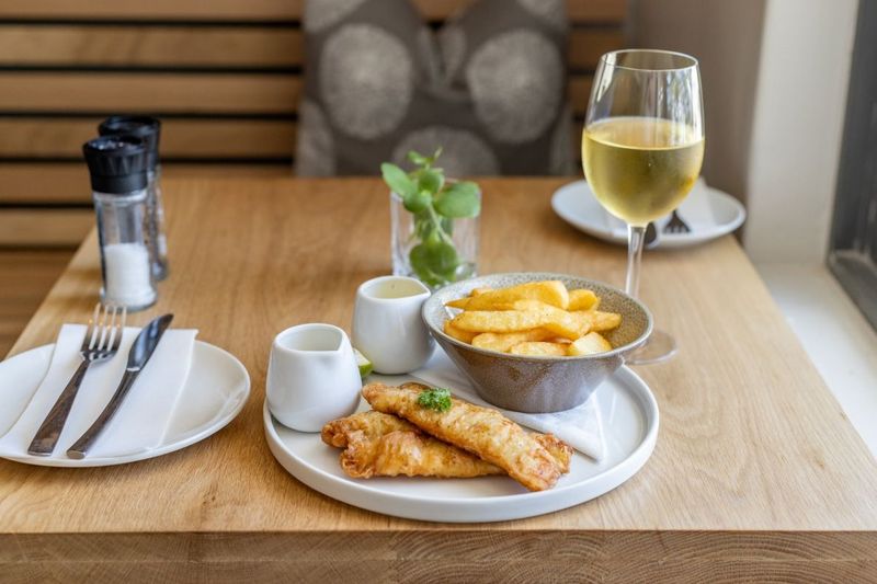 Crispy battered fish with a bowl of chips and a glass of white wine on a wooden table