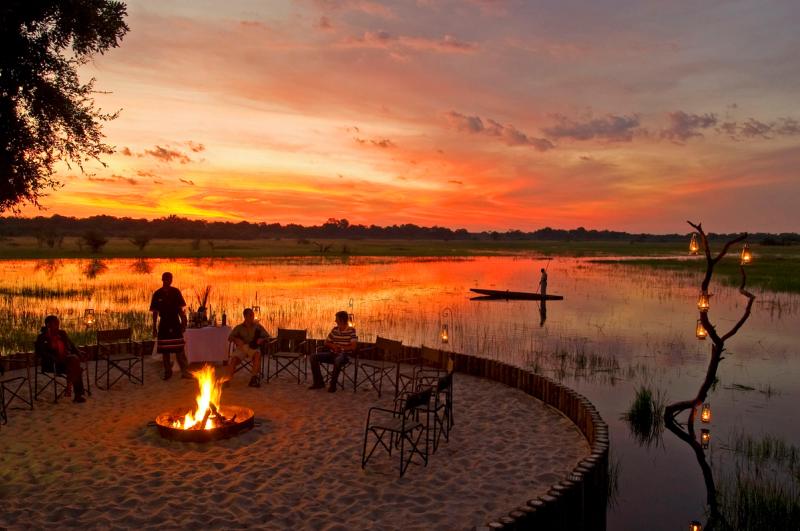 Guests enjoying sundowner drinks around a campfire next to the Delta at Sanctuary Chief's Camp