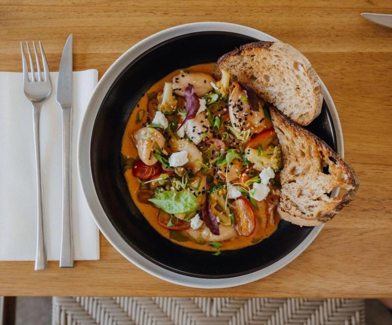 Black bowl of curried seafood and vegetables served with grilled sourdough bread slices