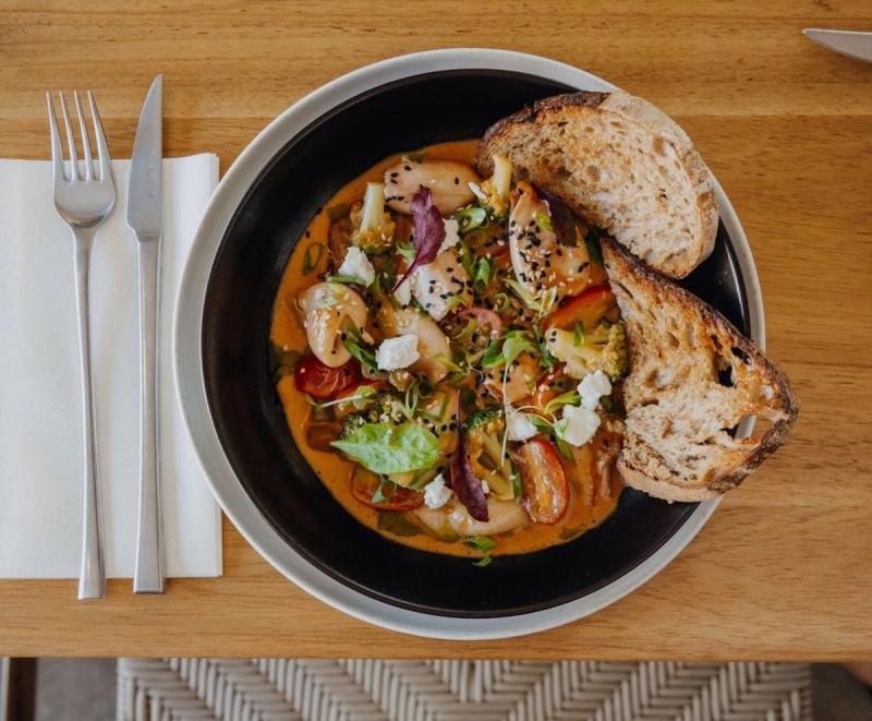 Black bowl of curried seafood and vegetables served with grilled sourdough bread slices