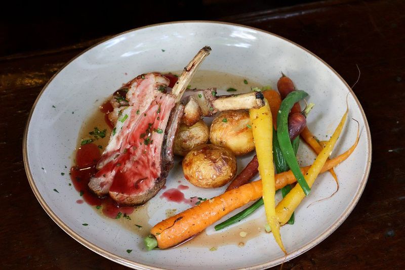 Sliced rack of lamb served with roasted potatoes and heirloom carrots on a white plate