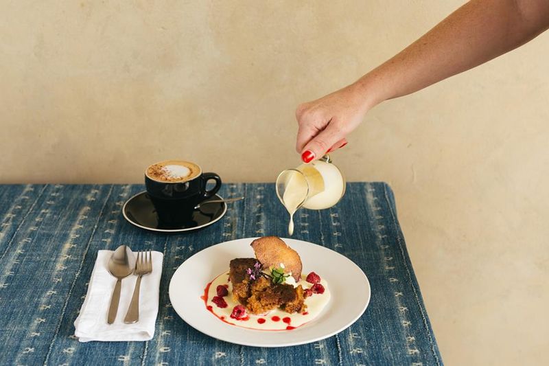 Frau gießt Vanillesoße über Malva Pudding