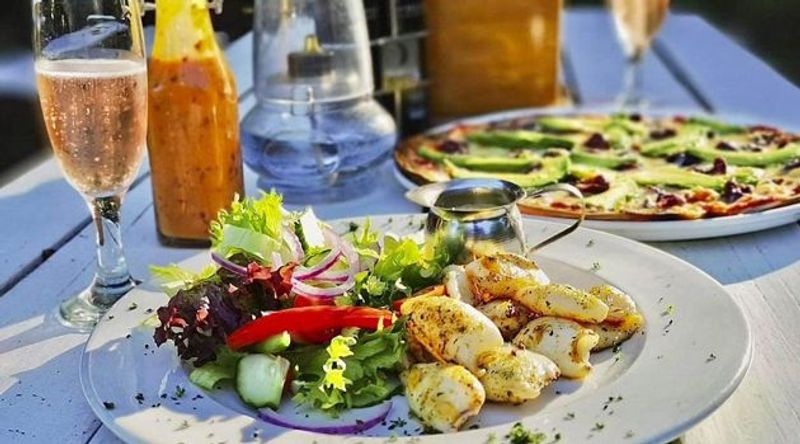 Plate of grilled calamari with fresh salad served alongside pizza and champagne outdoors