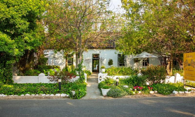 A white building entrance in Robertson surrounded by lush trees and a landscaped garden path.