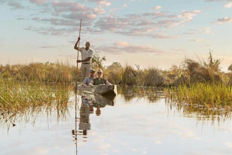 A guide poles a traditional mokoro canoe carrying two guests through calm channels during a safari in October