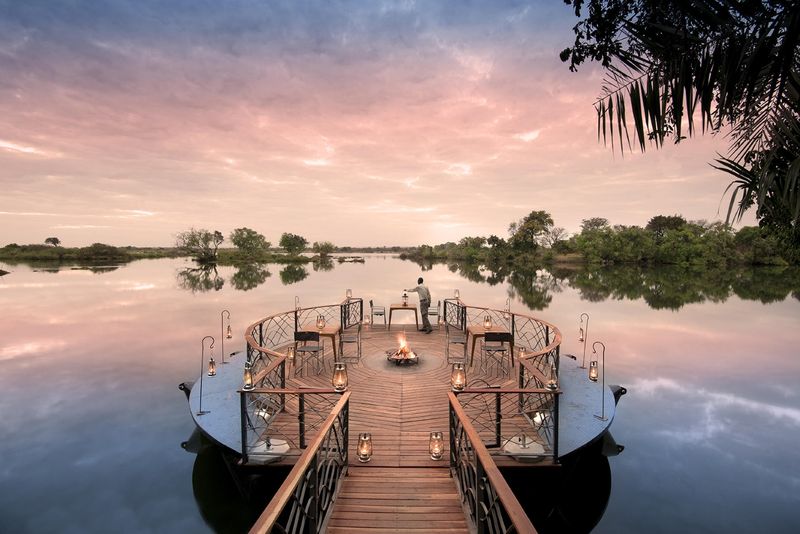 A breathtaking riverside deck adorned with lanterns and a cosy fire pit offers a tranquil setting for an intimate evening under a pastel sky