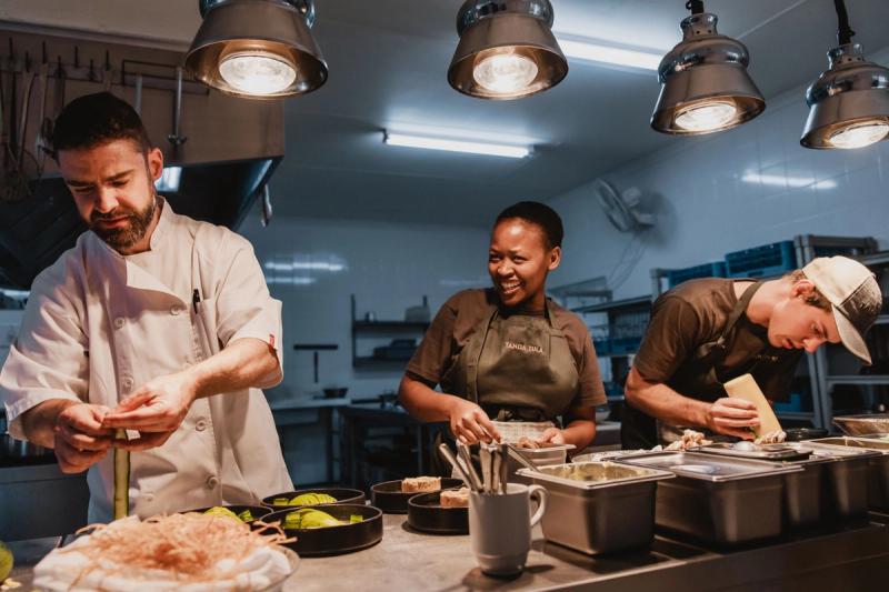 Three chefs working together preparing food at a stainless steel counter in a professional kitchen
