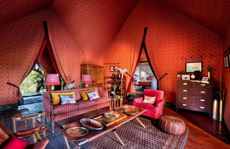 The colourful interior of a safari tent at Jack's Camp features patterned textiles, red furnishings and an open view of the surrounding wetland.