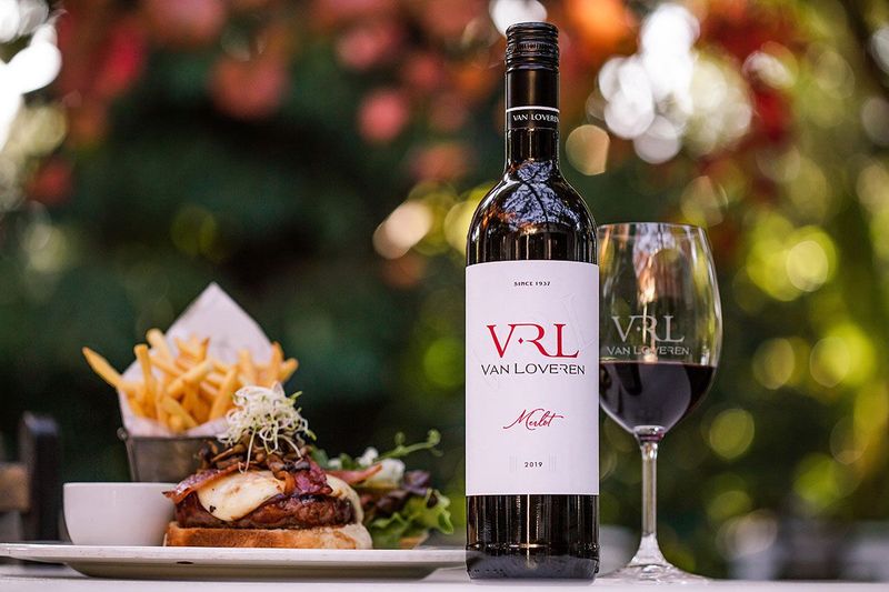 Bottle and glass of Van Loveren Merlot wine served beside a burger and fries