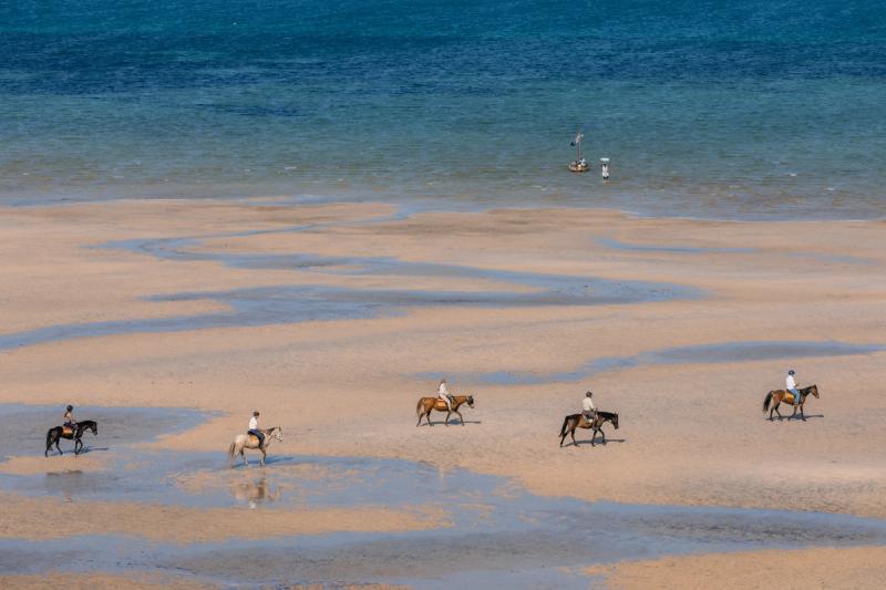 Horse riders crossing expansive tidal sandbanks along Mozambique’s coastline, with the blue Indian Ocean stretching into the distance.