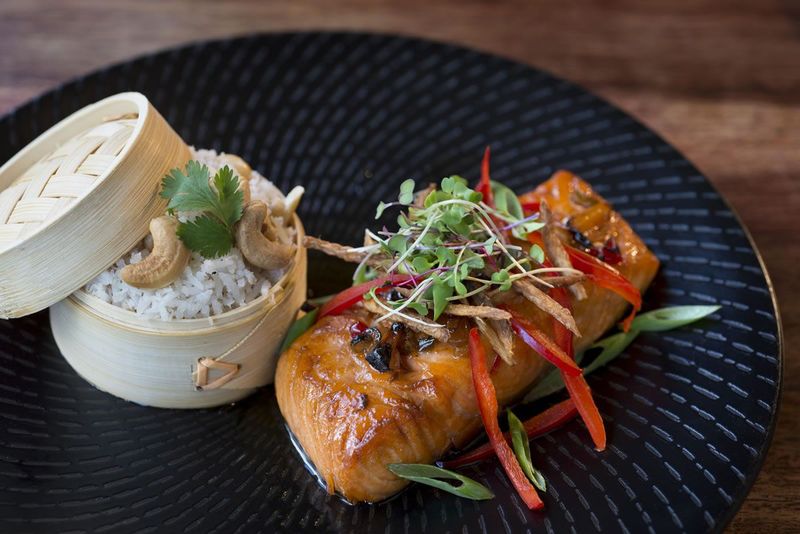 Glazed salmon fillet topped with microgreens served beside coconut rice in a bamboo steamer
