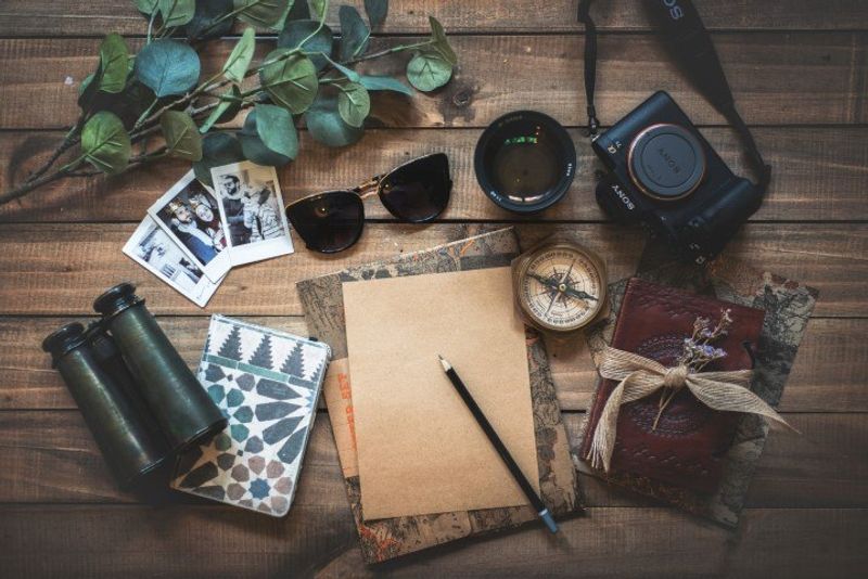 Auf einem Tisch liegen Reisedokumente, Sonnenbrille, Kompass, Kamera, Fotos und Schreibzubehör bereit
