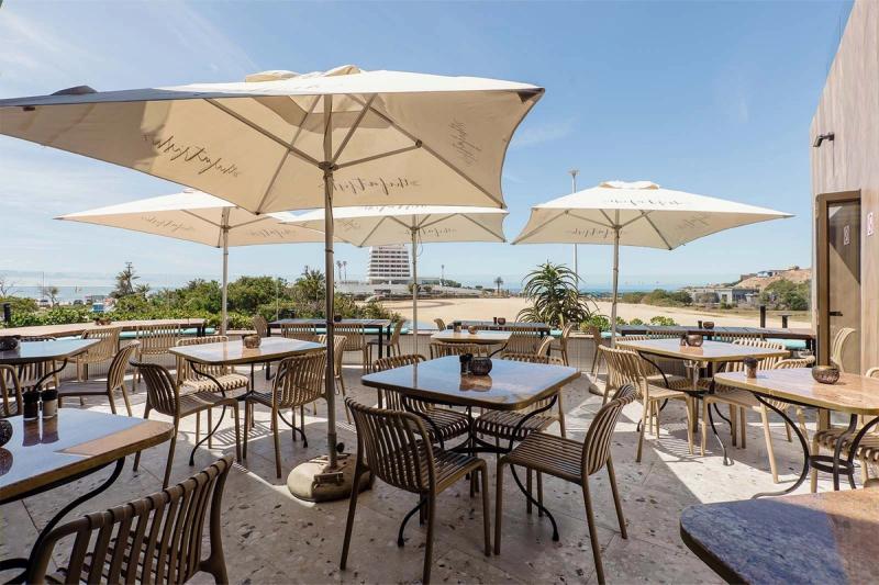 Outdoor dining terrace with large umbrellas and tables overlooking a beach and ocean in Plettenberg Bay