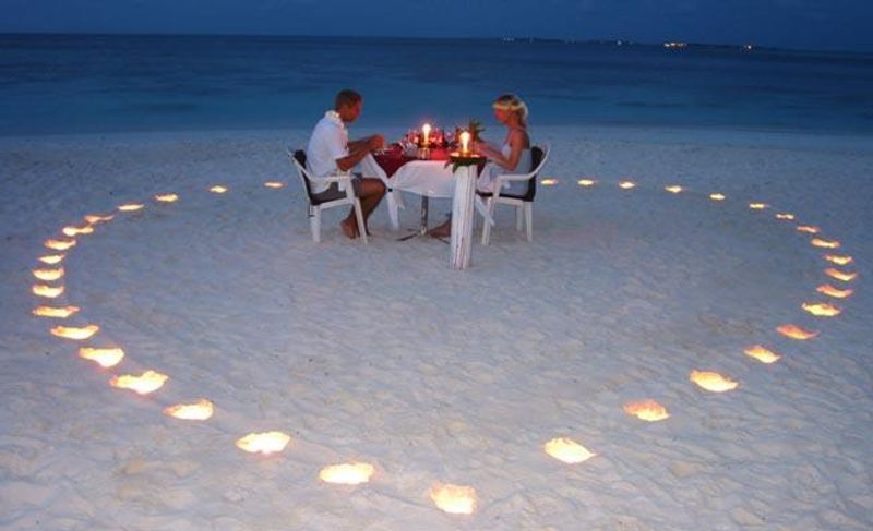 Ein Paar genießt ein romantisches Dinner am Strand umgeben von Kerzen, die ein Herz bilden