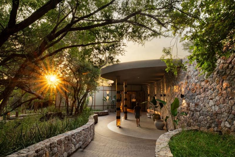 Stone-walled entrance with circular canopy and curved pathway surrounded by trees at sunset