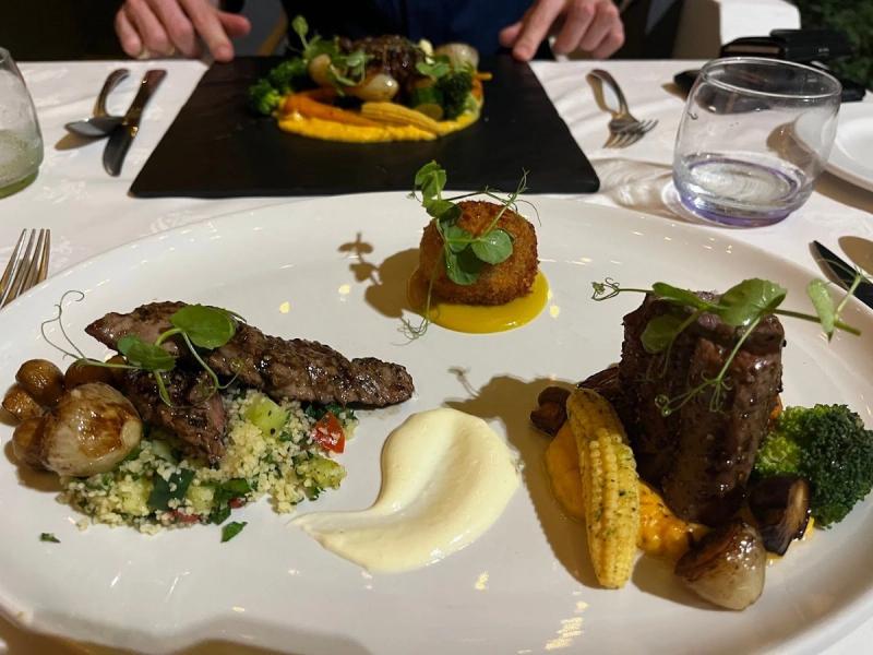 Plated steak with corn, broccoli, couscous and sauces on a fine dining table