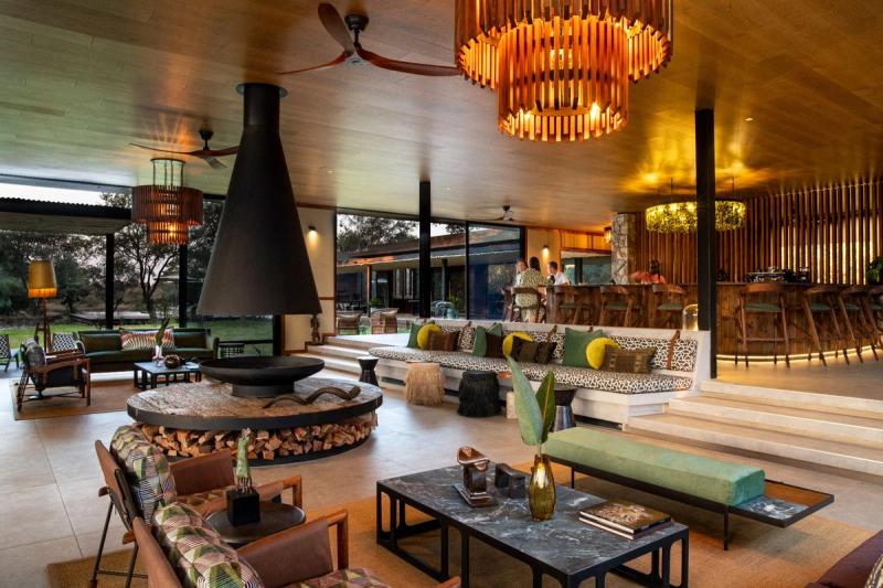 Spacious open-plan lounge with central fireplace, wooden chandeliers, and views to outdoor terrace at Timbavati Nature Reserve