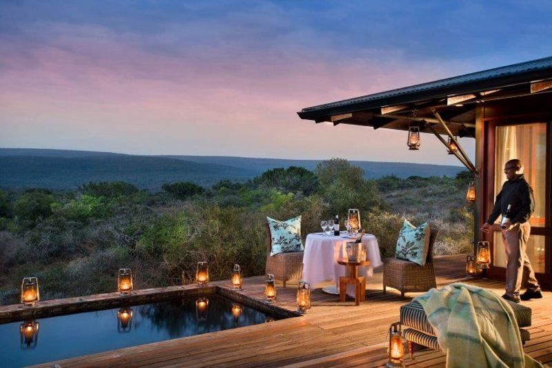 Ein gedeckter Tisch neben einem Pool in einer Suite der Kwandwe Ecca Lodge bei Sonnenuntergang
