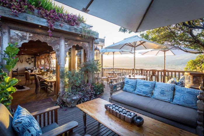 Covered wooden deck with sofa and umbrellas overlooking hills and ocean in Plettenberg Bay