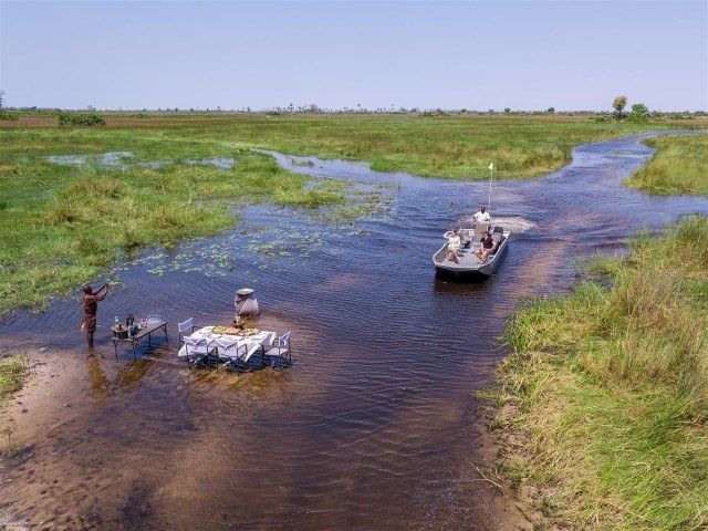 Ein Mann steht neben einem gedeckten Tisch im seichten Wasser und wartet auf ein Boot, das sich ihm nähert