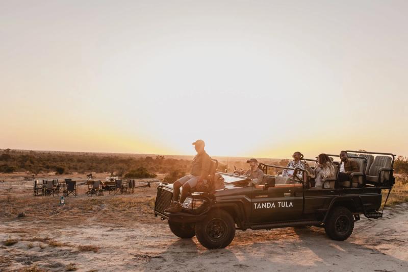 Safari vehicle stopped at sunset with guests and chairs set up for a bush sundowner in African savanna