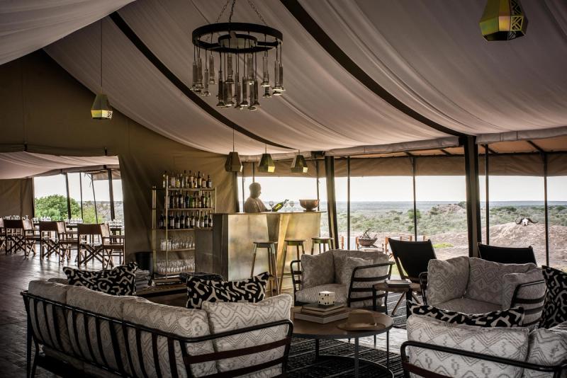 A fully furnished lounge and bar setup inside one of Africa’s mobile tented camps, complete with chandeliers, drinks service, and panoramic views.