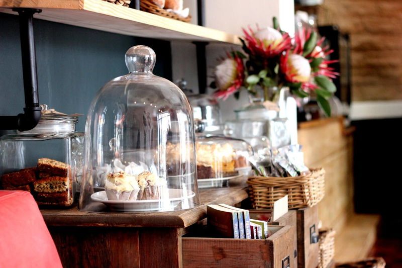 Glass dome covers pastries on a counter with protea flowers and woven baskets