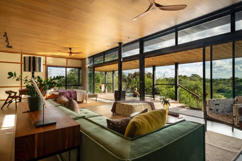 Open plan living room with green sofas and floor-to-ceiling windows overlooking bushveld landscape