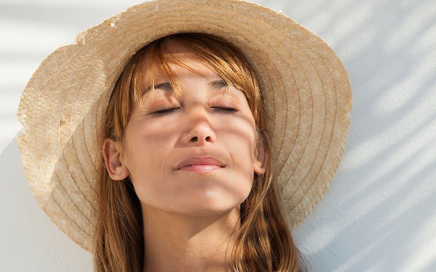 Dame md stråhatt som lukker øynene mot solstriper filtrert gjennom blader