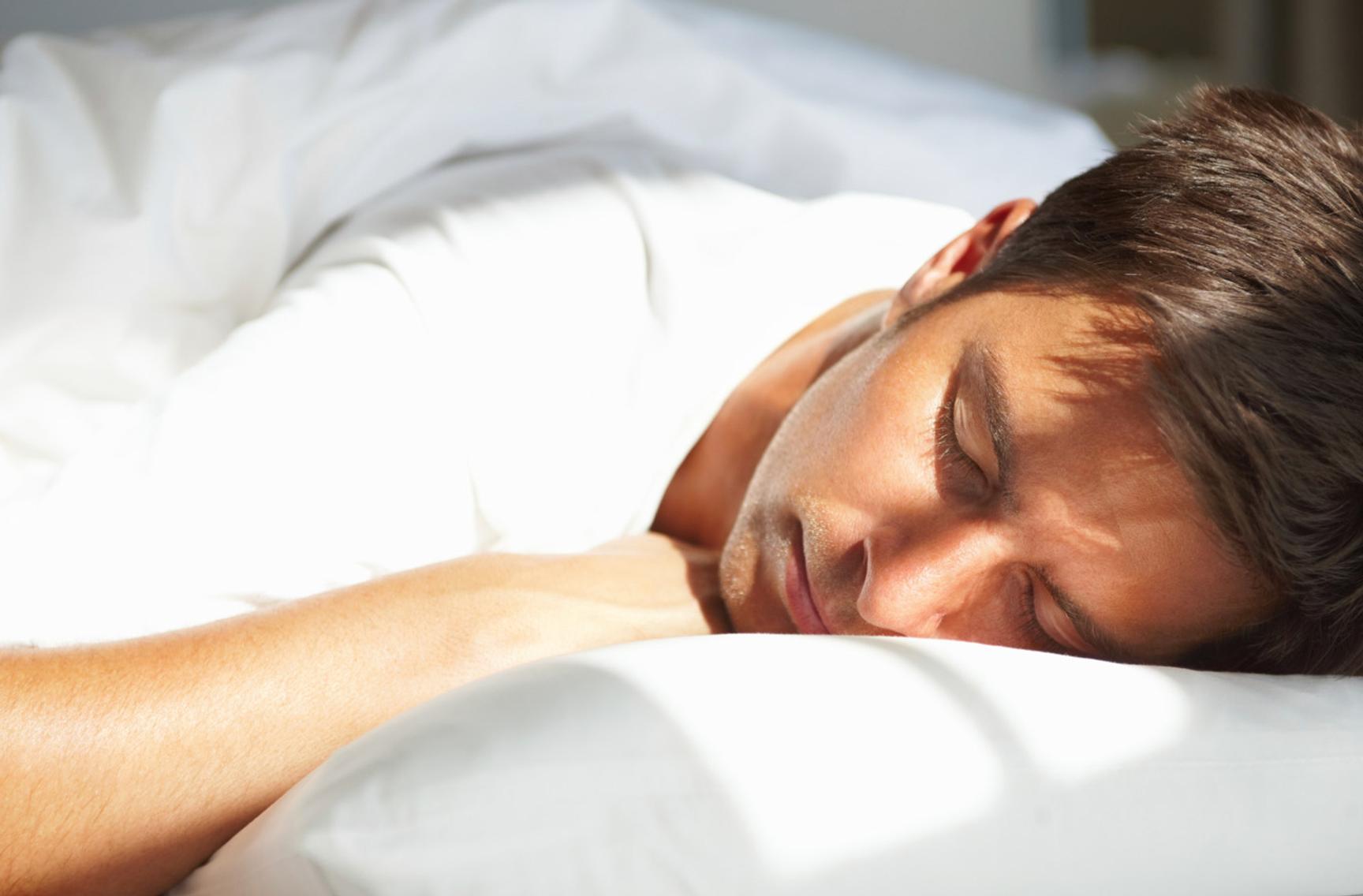 Mann ligger i seng med lukkede øyne