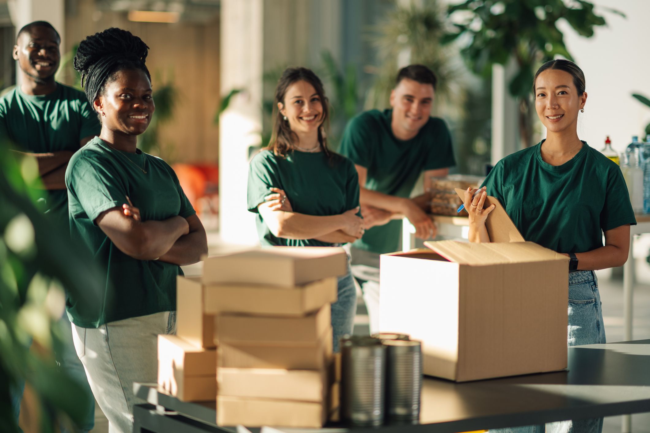 5 grønnkledde personer pakker varer i esker og smiler mot kamera