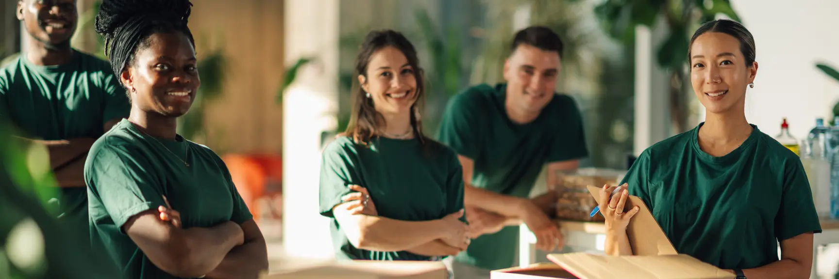 5 grønnkledde personer pakker varer i esker og smiler mot kamera