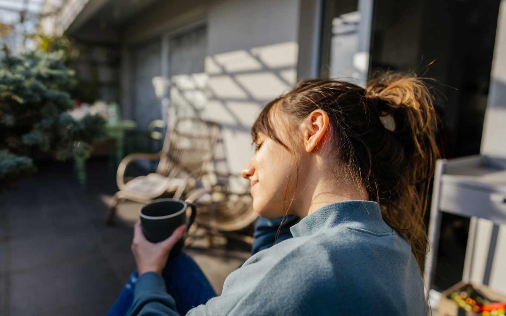 En kvinne nyter en kopp kaffe i solveggen